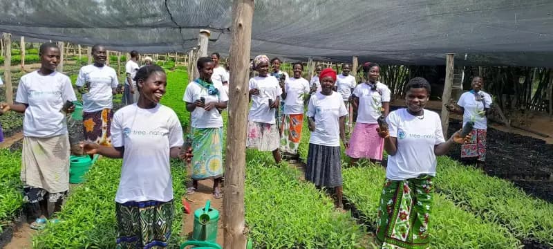A group of women and children in a tree nursery, the women holding up young seedlings.